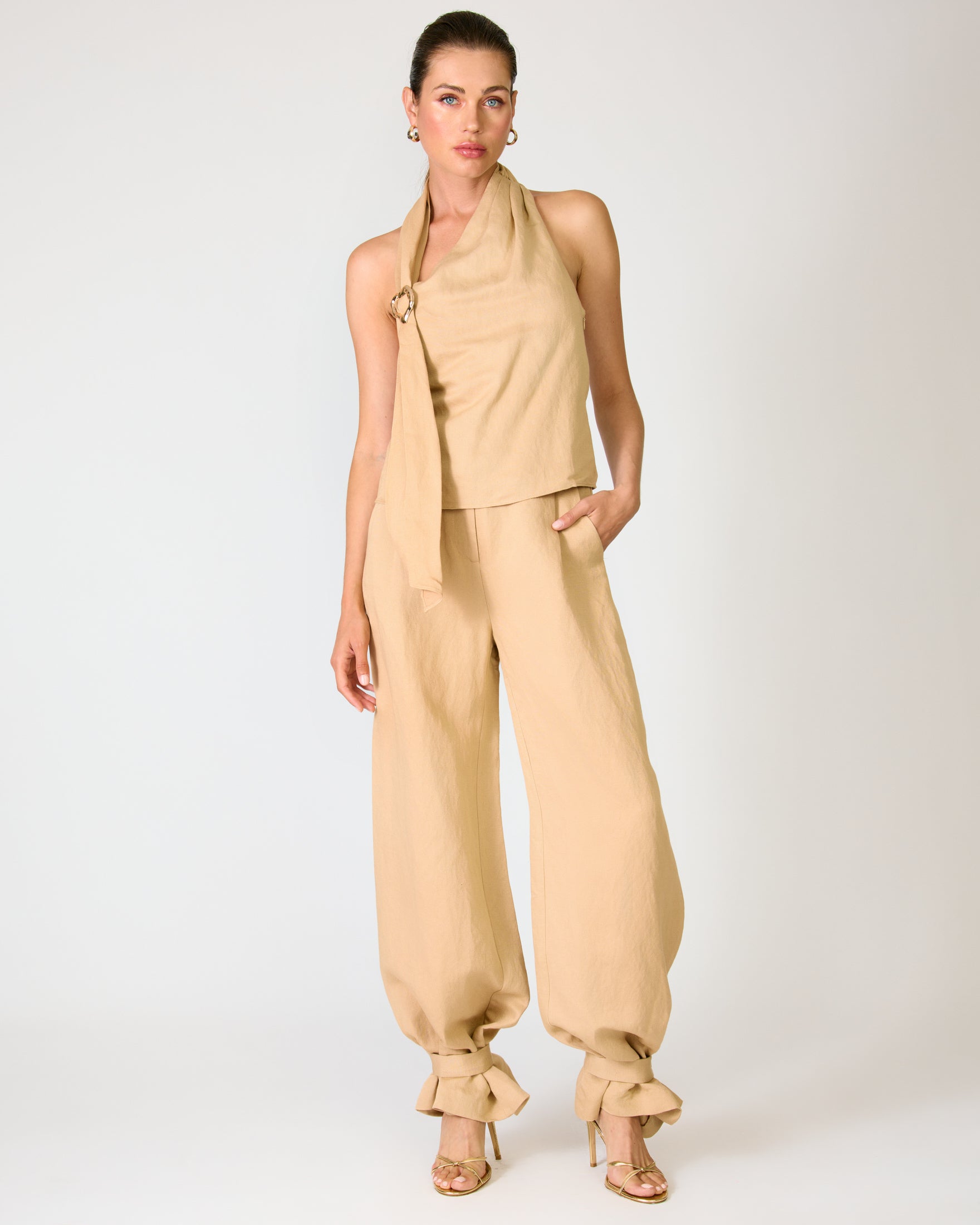 Woman wearing a beige halter top and wide-leg pants on a white background