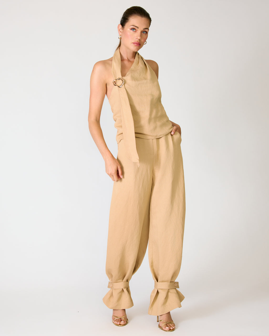 Woman wearing a beige halter top and tapered-leg pants on a white background