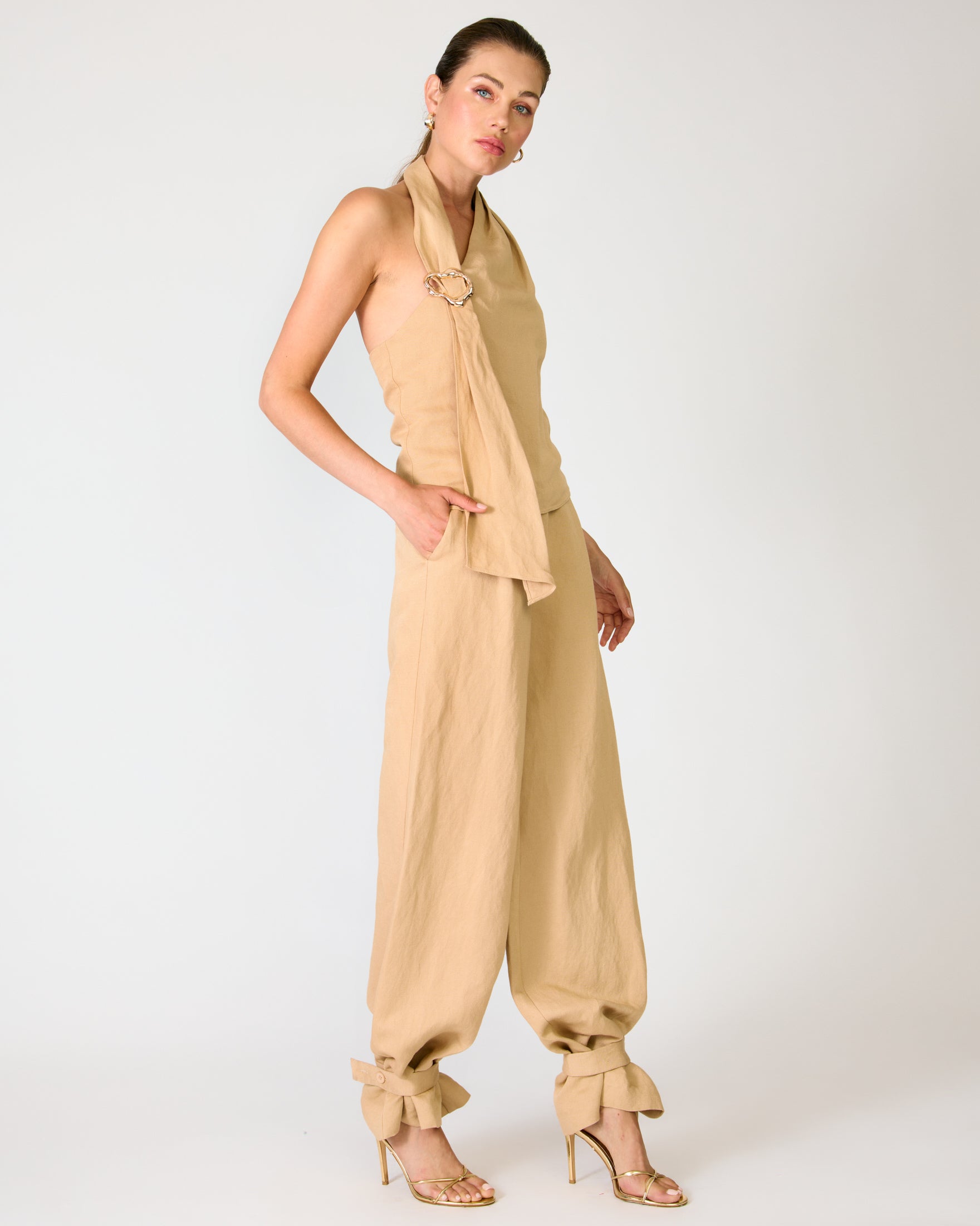Woman wearing a beige halter top and tapered-leg pants on a white background