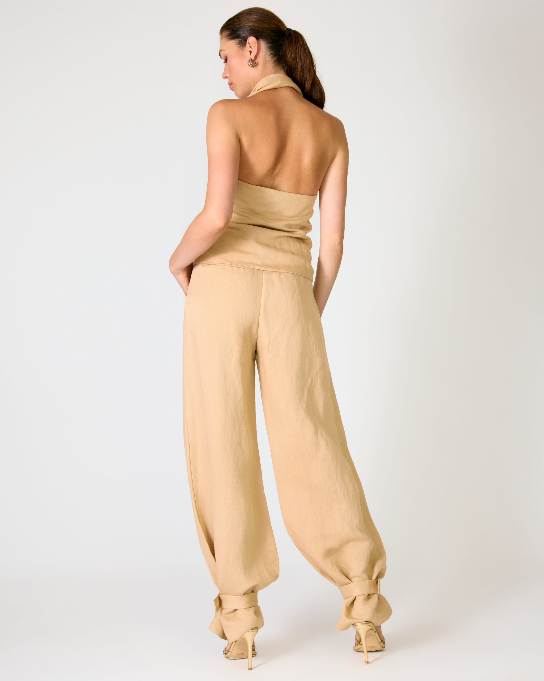 Woman wearing a beige halter top and tapered-leg pants on a white background